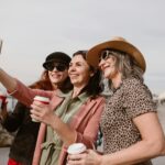 Three women enjoying coffee and taking a selfie together seaside.