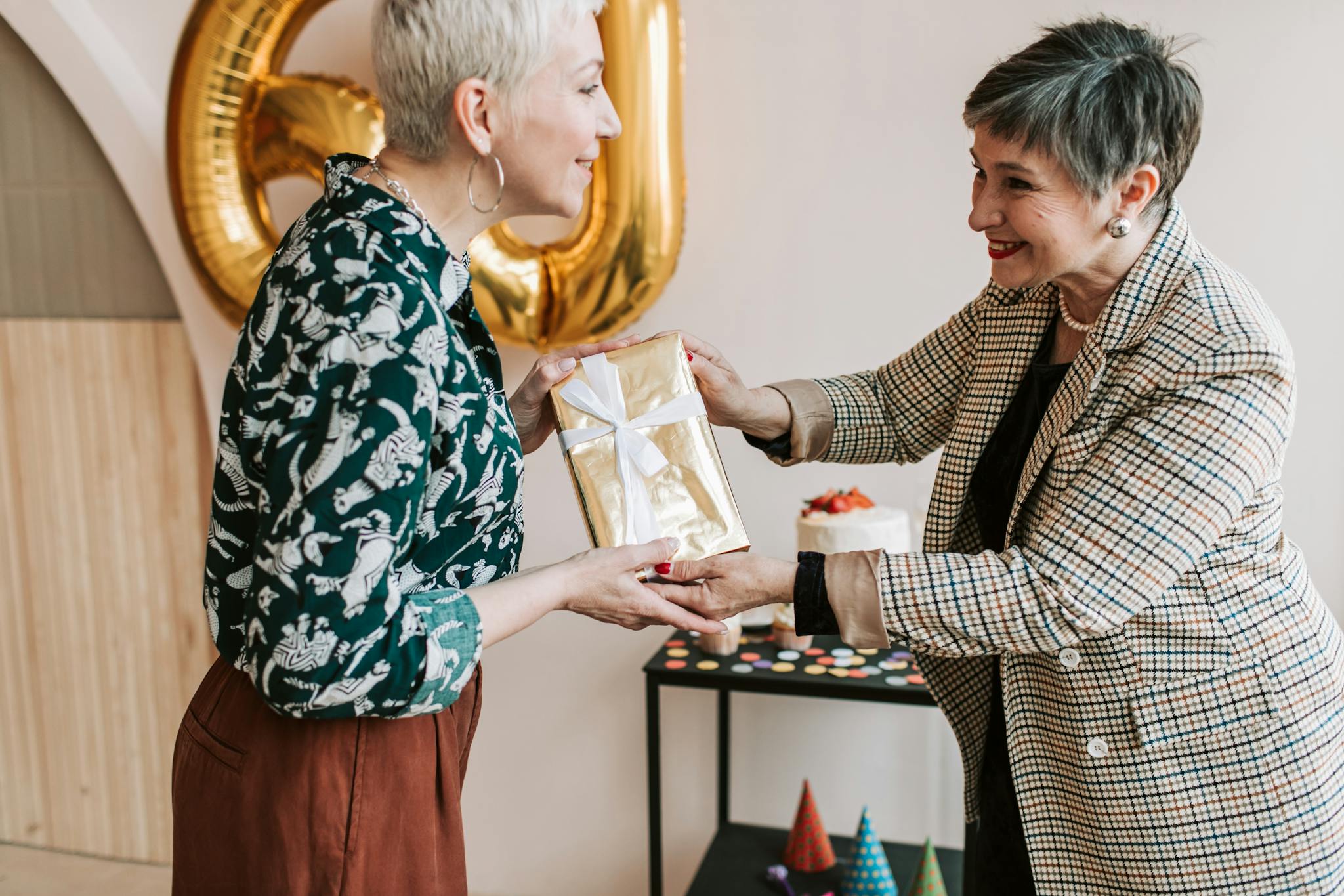 Two senior women exchanging a gift at a joyous indoor birthday celebration.